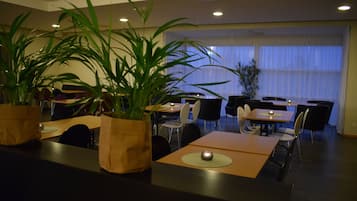 Un comedor con mesas, sillas y plantas en macetas.