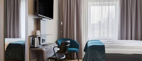 A hotel room with a bed, a desk with a chair, a television, and a window with curtains.