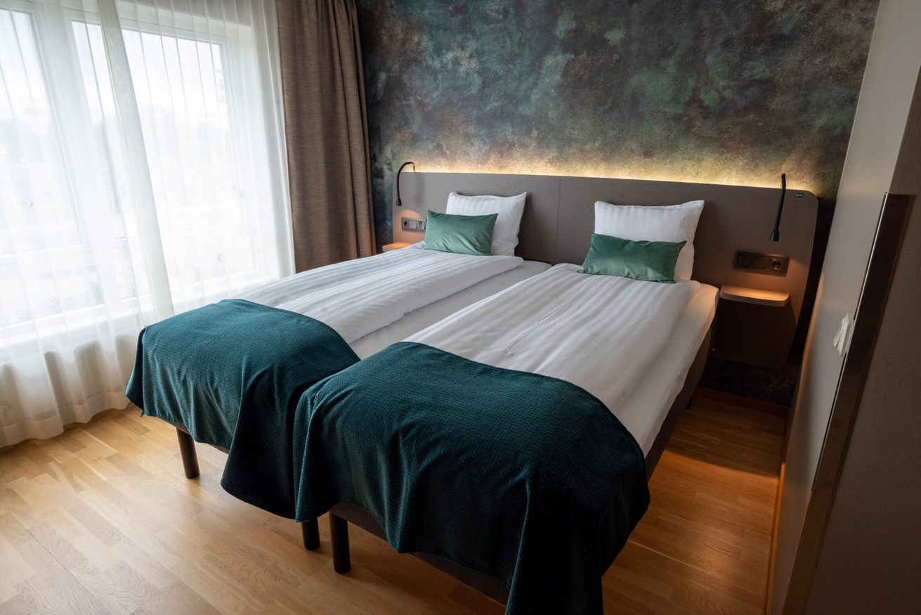 En dobbeltseng med to puder, et sengebord og en vægmonteret lampe.