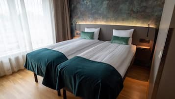 En dobbeltseng med to puder, et sengebord og en vægmonteret lampe.