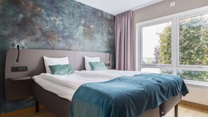 Un dormitorio moderno con una cama grande, una mesita de noche, una lámpara de pared y una ventana con vistas a árboles.