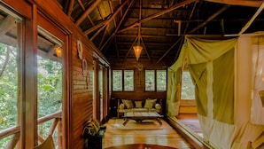 A wooden cabin with a sofa, a dining table with a vase, and a tent-like structure.
