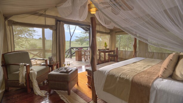 A tented accommodation with a bed, seating area, and a view of the outdoors.