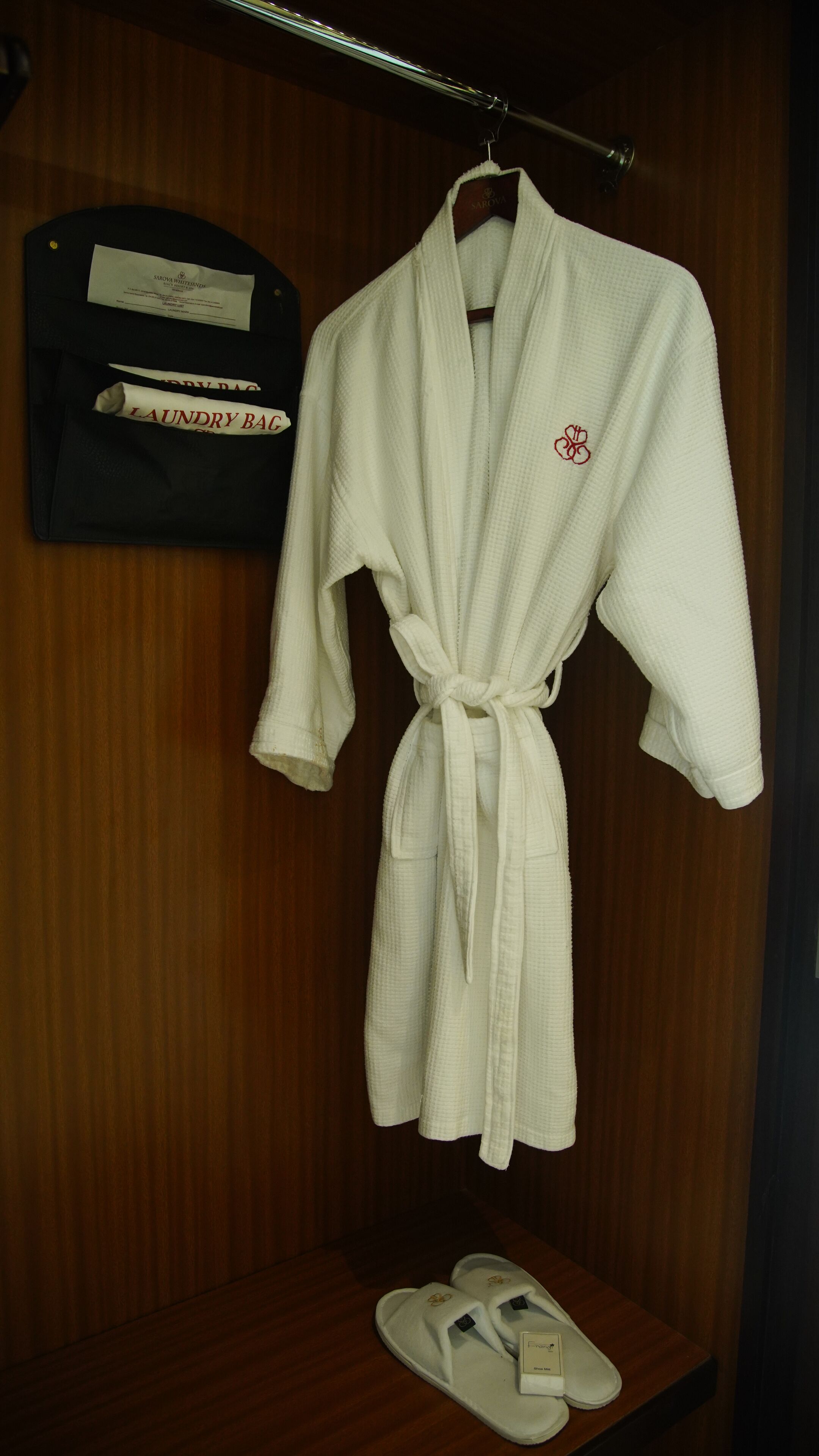 A white robe hanging on a wooden hanger in a wooden closet with a wooden shelf below it.