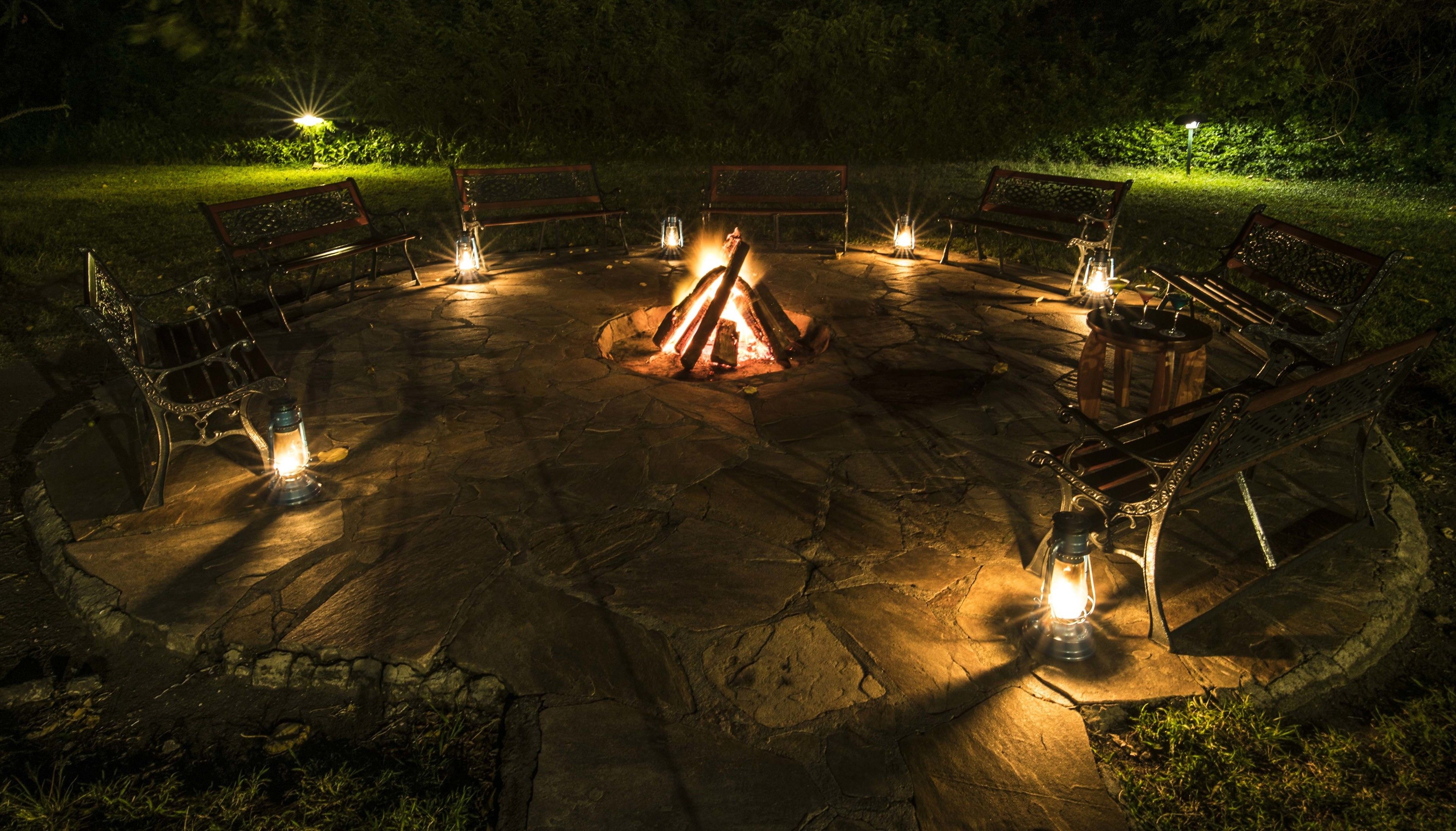 A circular stone fire pit with benches around it, surrounded by lanterns.