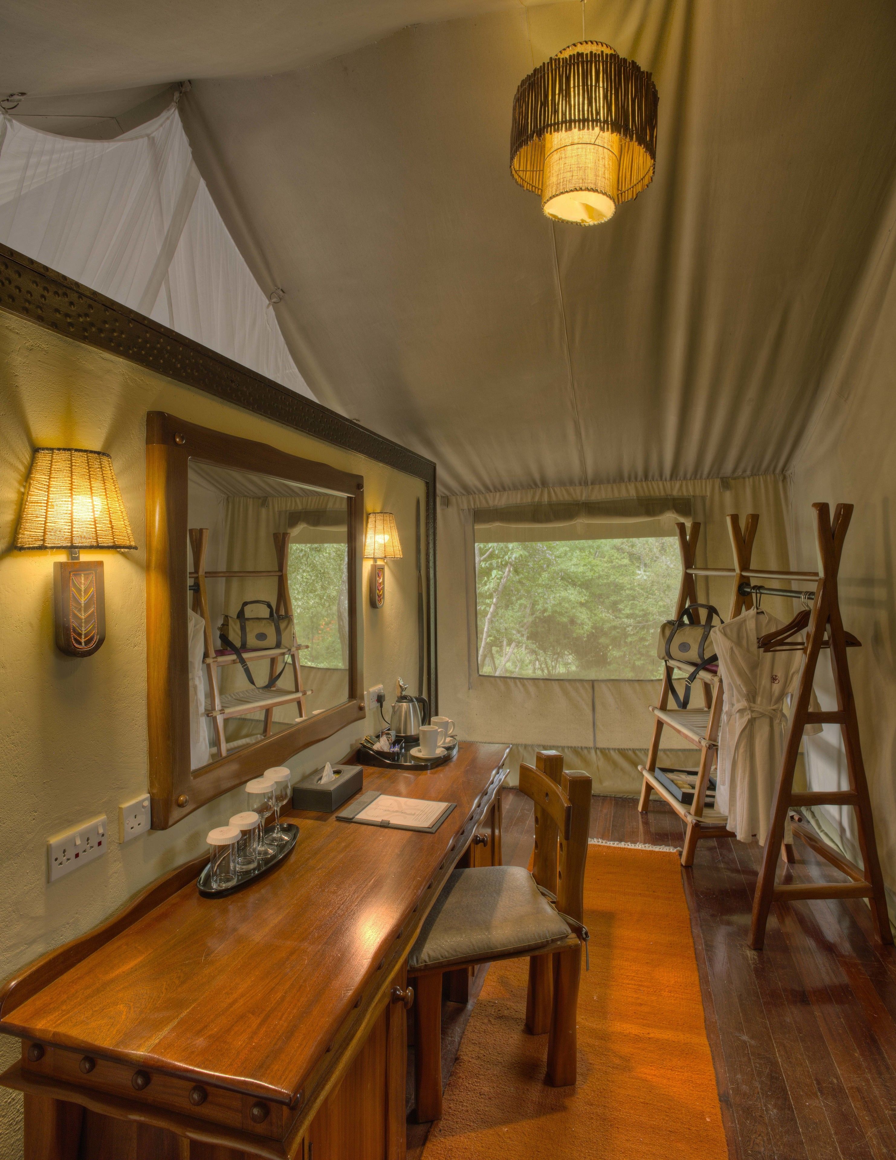 A tented room with a wooden dining table, chairs, a chandelier, and a large mirror.