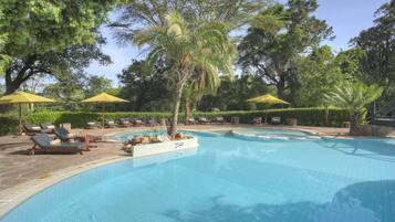 Una piscina con sillas de descanso y sombrillas, rodeada de árboles.
