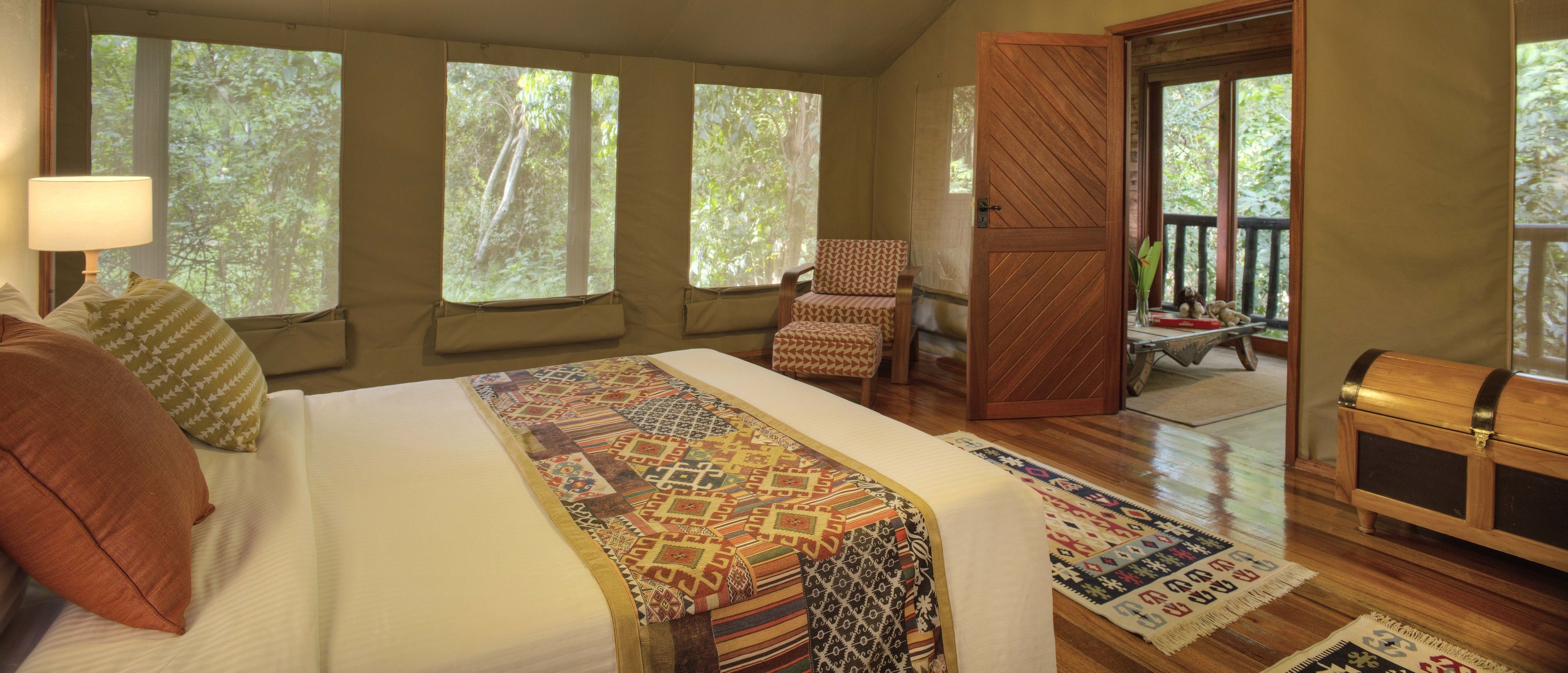 A bedroom with a large bed, multiple windows, a chair, a wooden chest, and a view of the outdoors.