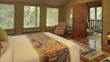 A bedroom with a large bed, multiple windows, a chair, a wooden chest, and a view of the outdoors.