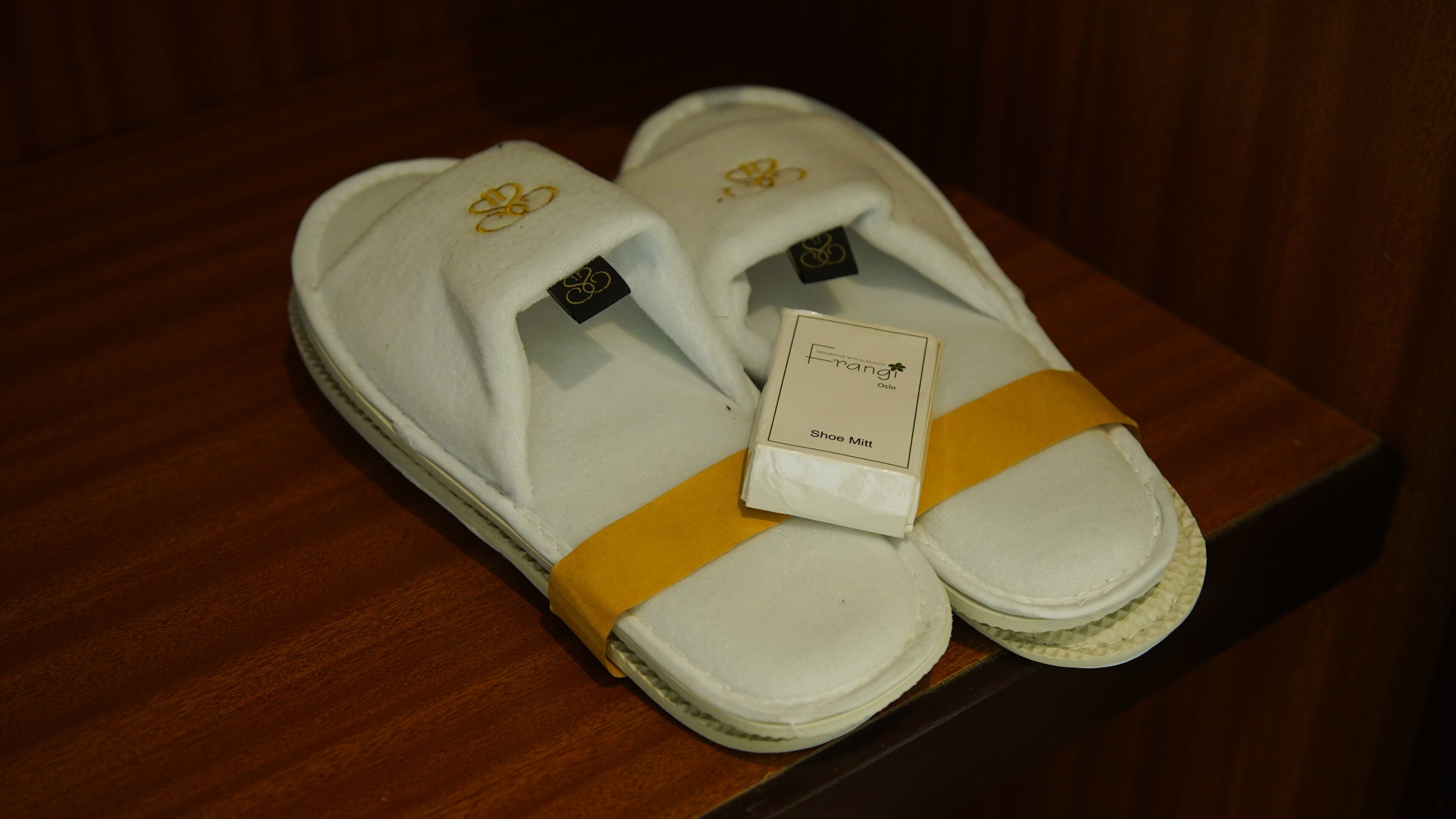 Un par de zapatillas blancas con detalles amarillos y una etiqueta que dice 'Frang Oslo Shoe Mitt'.