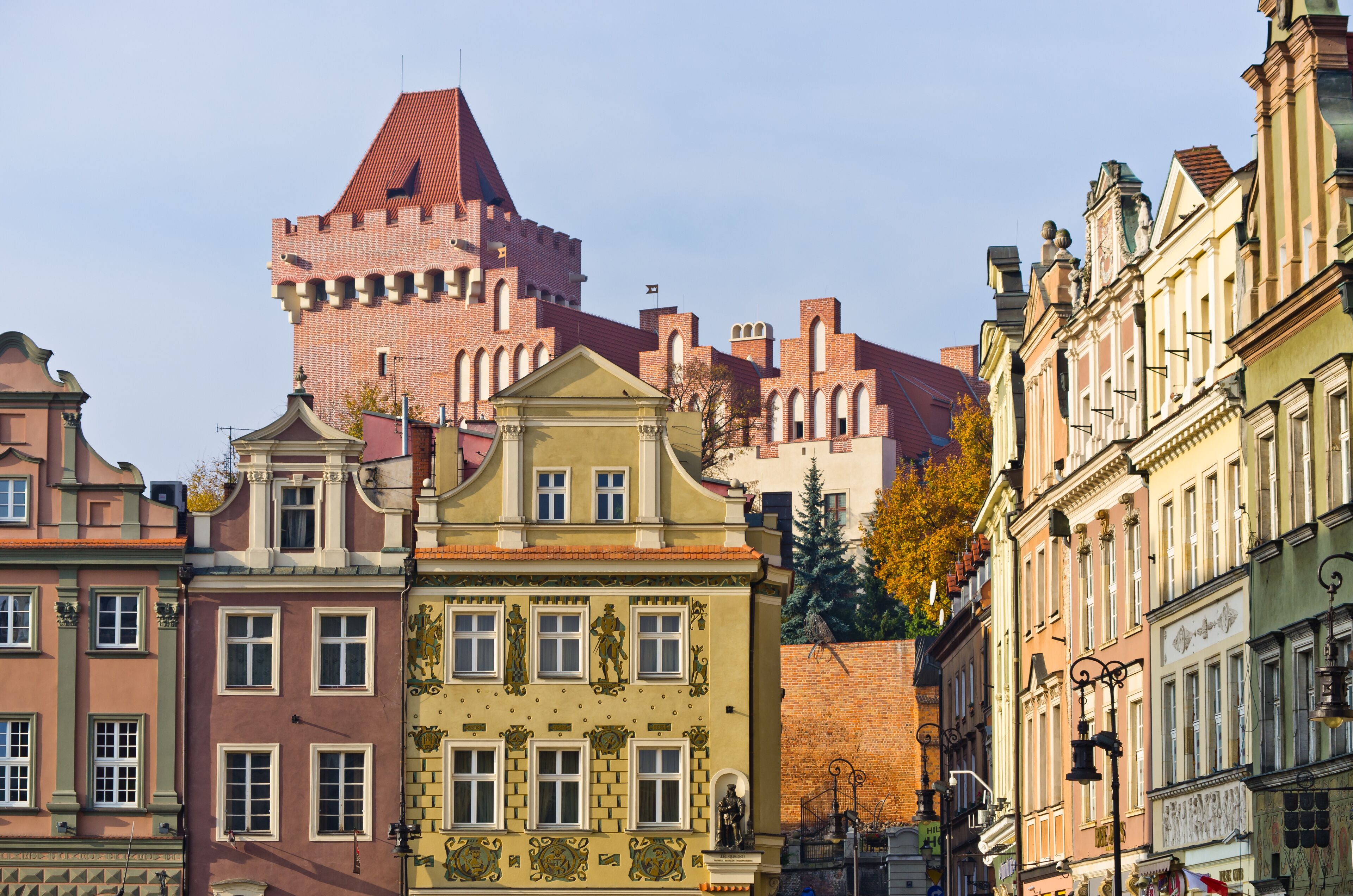 Un bâtiment historique doté d’une tour imposante et d’un toit rouge, entouré d’immeubles aux façades colorées et aux styles architecturaux variés.