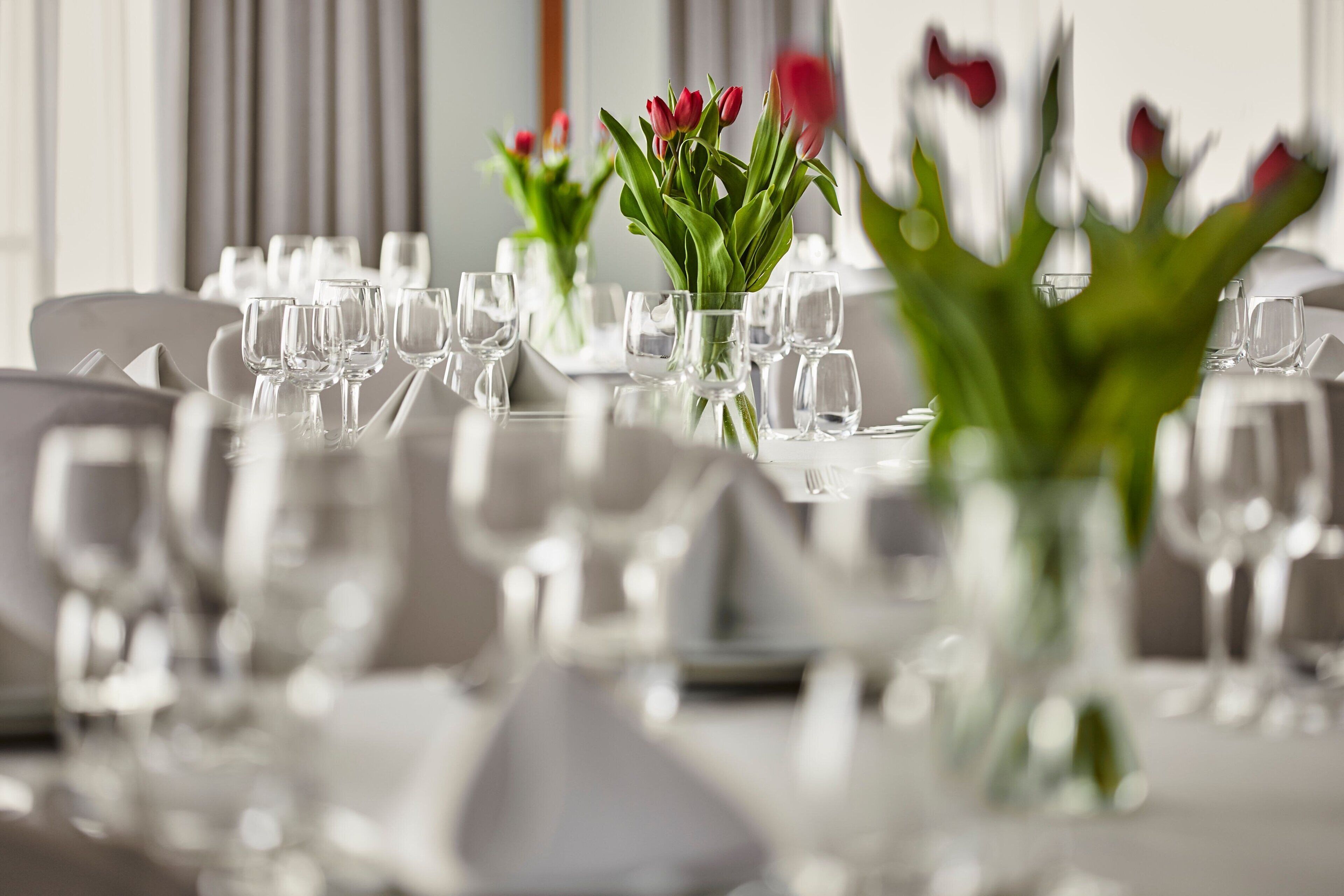 A dining table set with multiple glasses and a vase of red tulips.