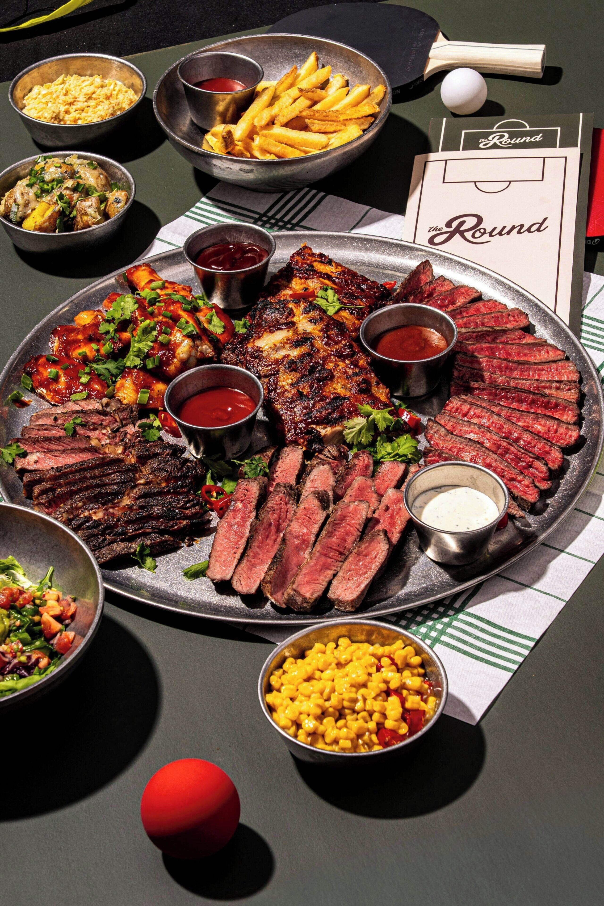 A round table with a variety of dishes including steak, fries, and a salad.