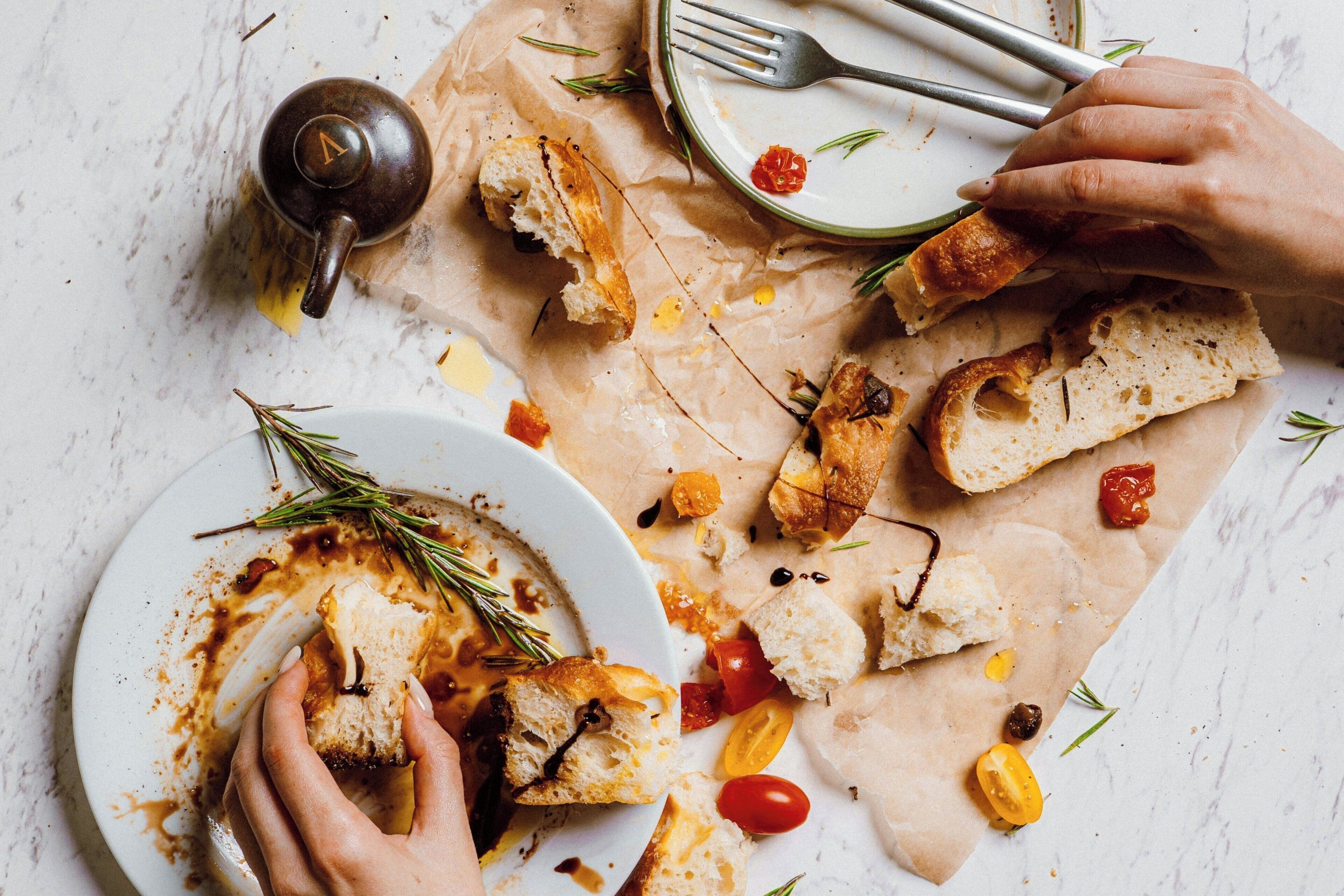A dining table with a plate of bread and tomatoes, a teapot, and a fork.