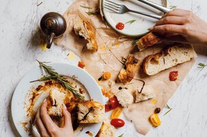 A dining table with a plate of bread and tomatoes, a teapot, and a fork.