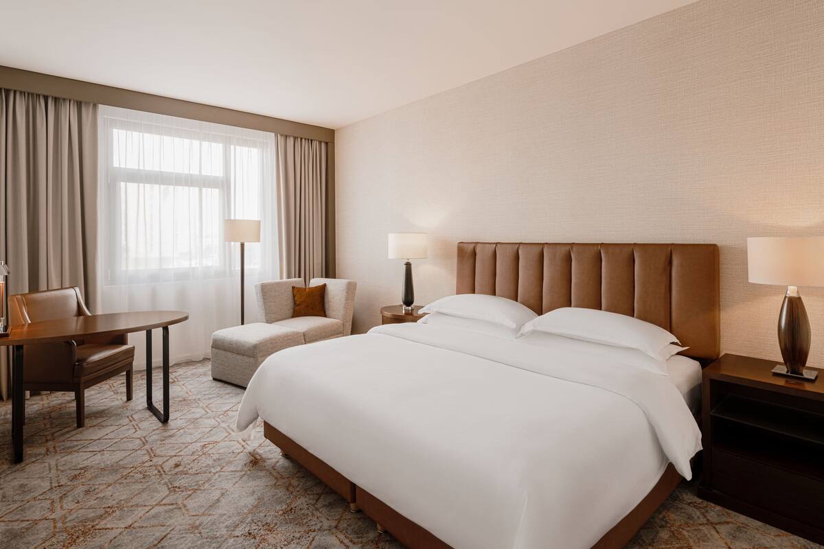 Ein Hotelzimmer mit einem großen Bett, einem Schreibtisch, einem Stuhl und einem Nachttisch mit Lampen.
