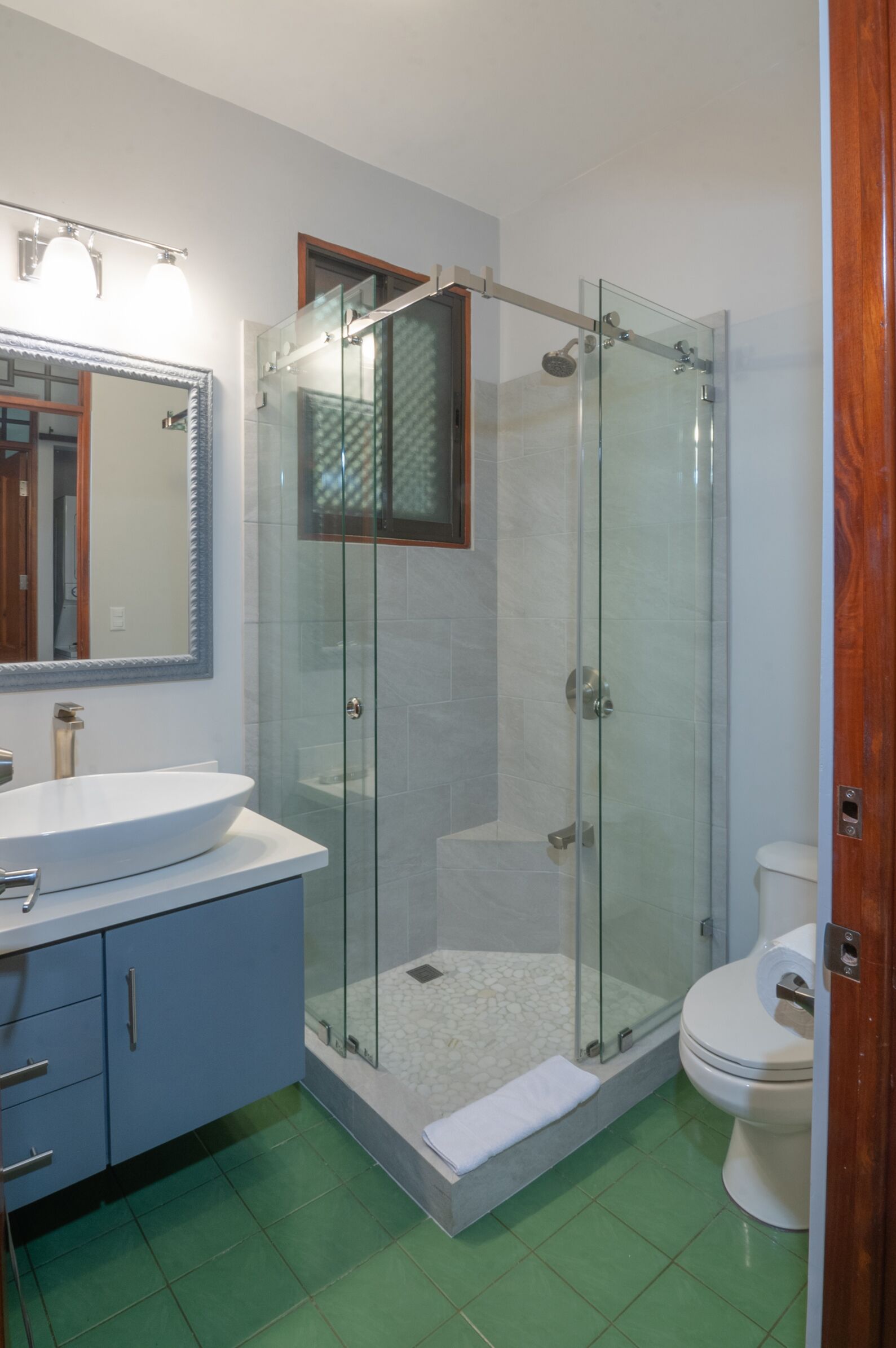 Un baño con ducha de vidrio, lavamanos con espejo e inodoro.