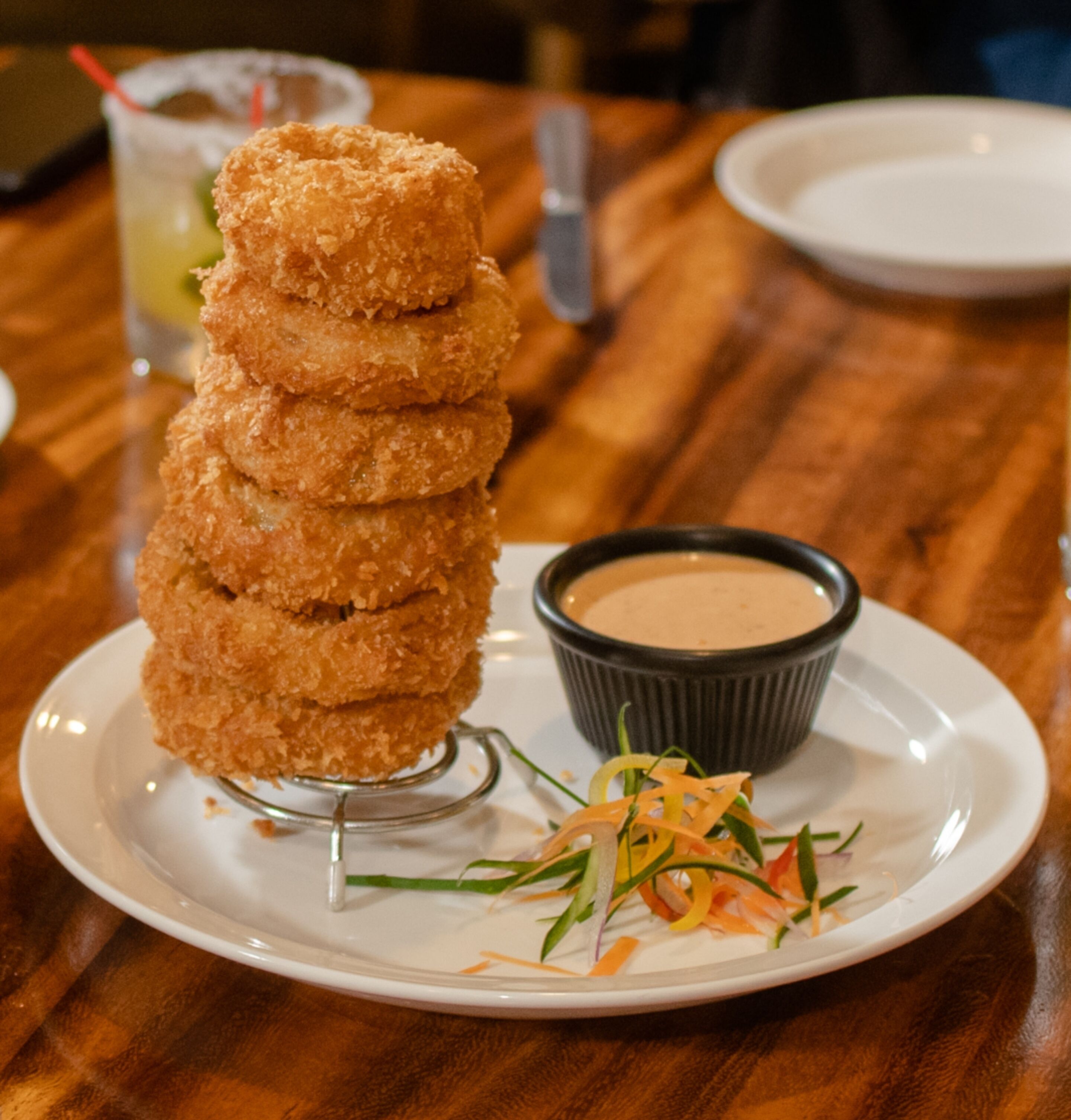 A stack of breaded items on a plate with a dipping sauce and a side salad.