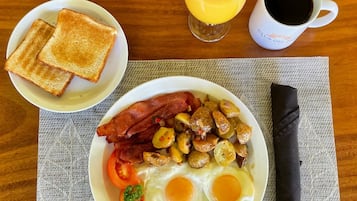 Prato de café da manhã com ovos, bacon, batatas e torradas, acompanhado de um copo de suco de laranja e uma xícara de café.
