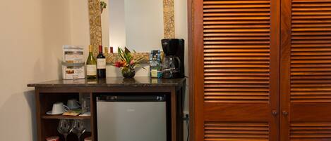 Una cocina con refrigerador, cafetera y una alacena con botellas de vino y copas.