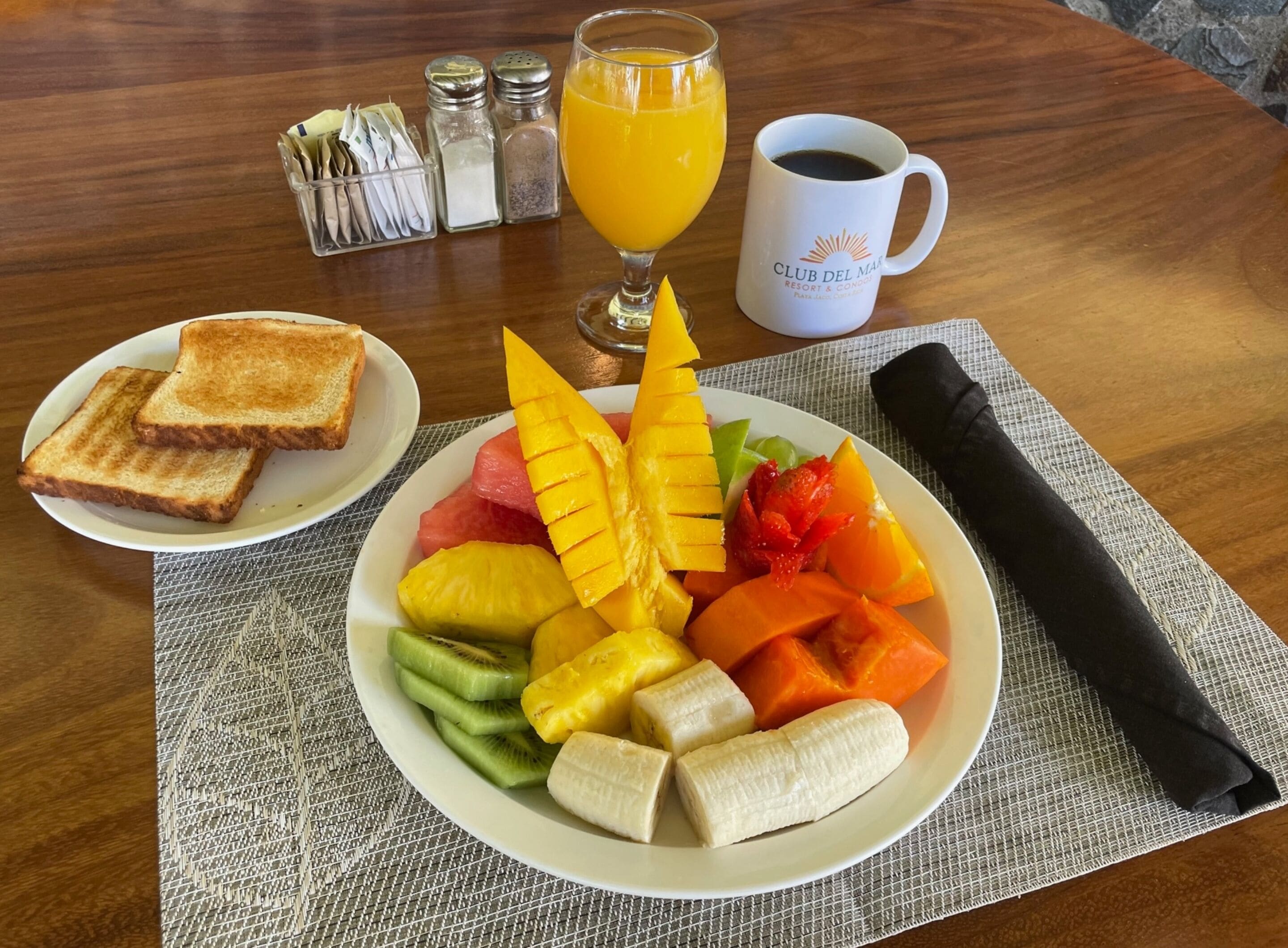 A breakfast plate with toast, fruit, and a glass of orange juice on a wooden table.