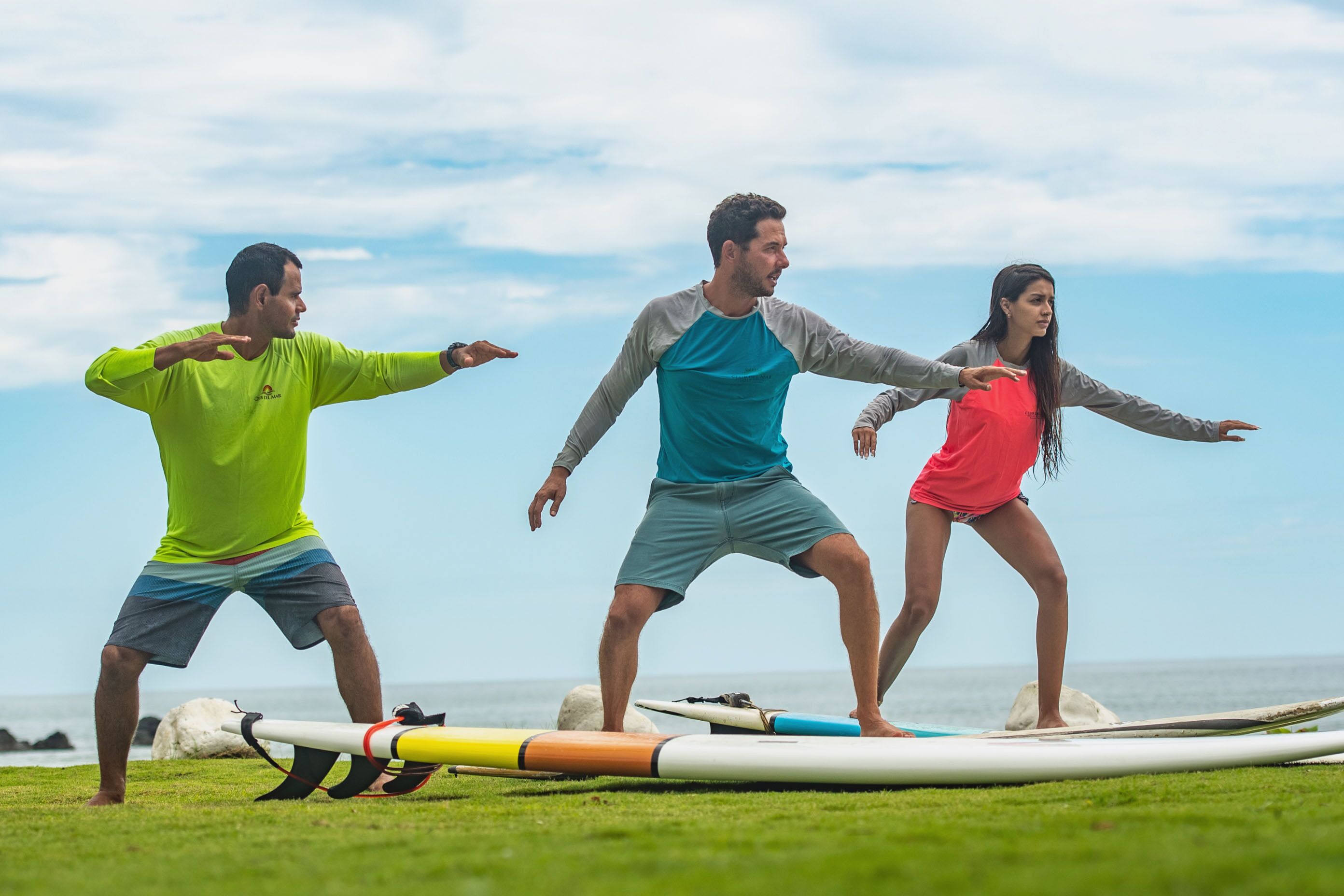 Three people practicing on surfboards on a grassy area by the ocean.