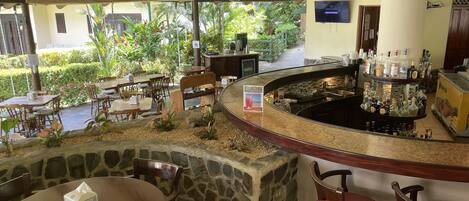 A bar area with a stone counter, wooden chairs, and a view of a garden with various plants and a pathway.