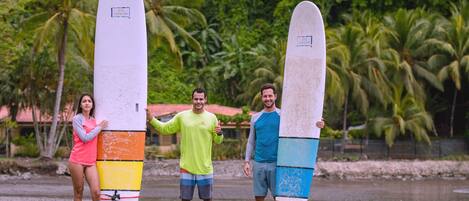 Three people holding surfboards on a beach with palm trees in the background.