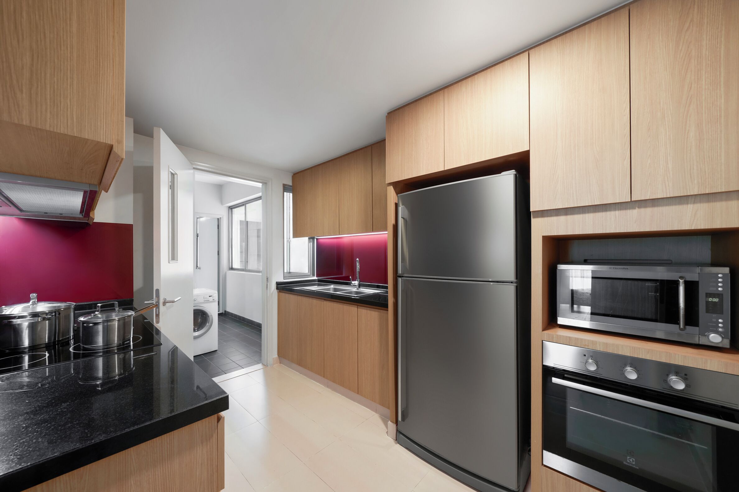 A modern kitchen with wooden cabinets, a stainless steel refrigerator, a microwave, and an oven.