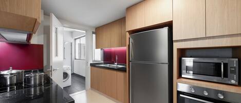 A modern kitchen with wooden cabinets, a stainless steel refrigerator, a microwave, and an oven.