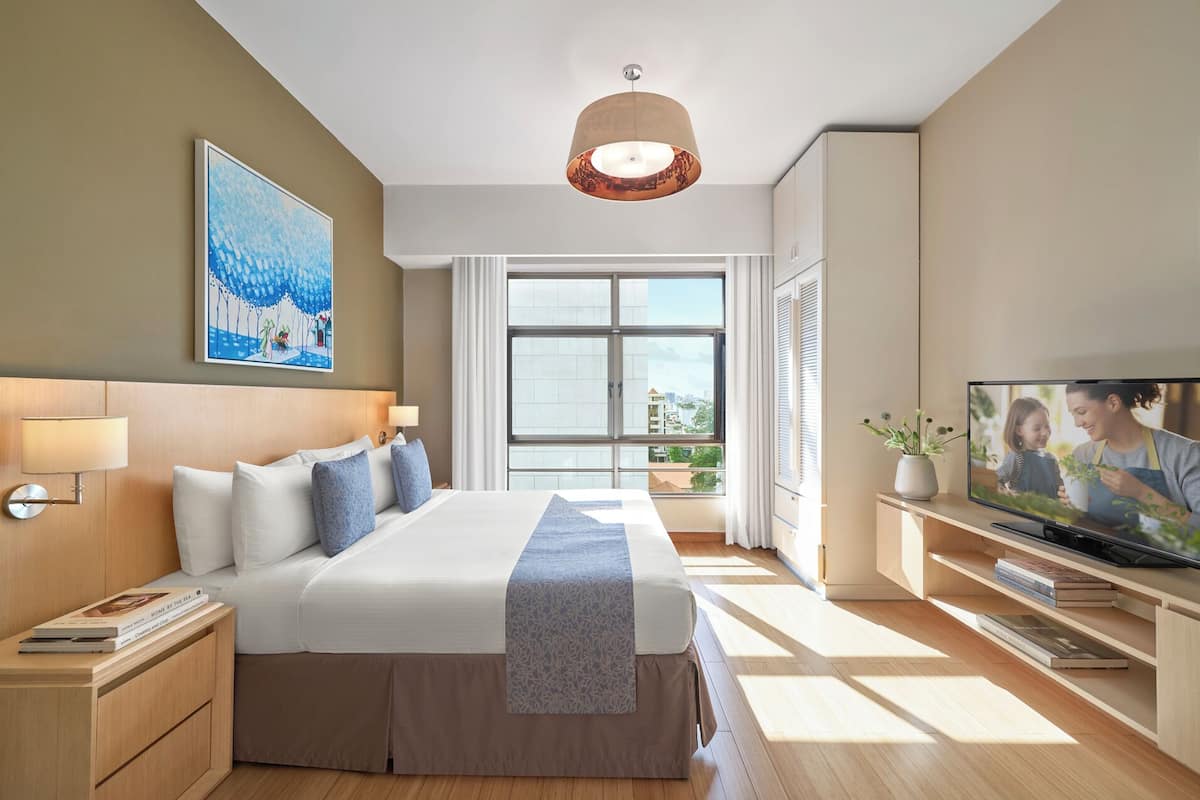 Una habitación de hotel moderna con una cama grande, televisión y ventana con vista a la ciudad.