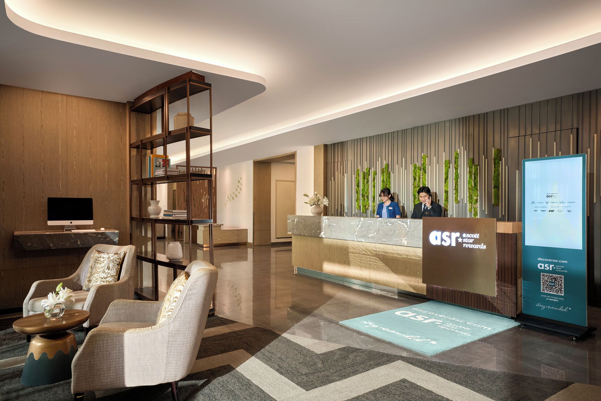 A modern reception area with a marble counter, a digital screen, and a seating area with a patterned rug.