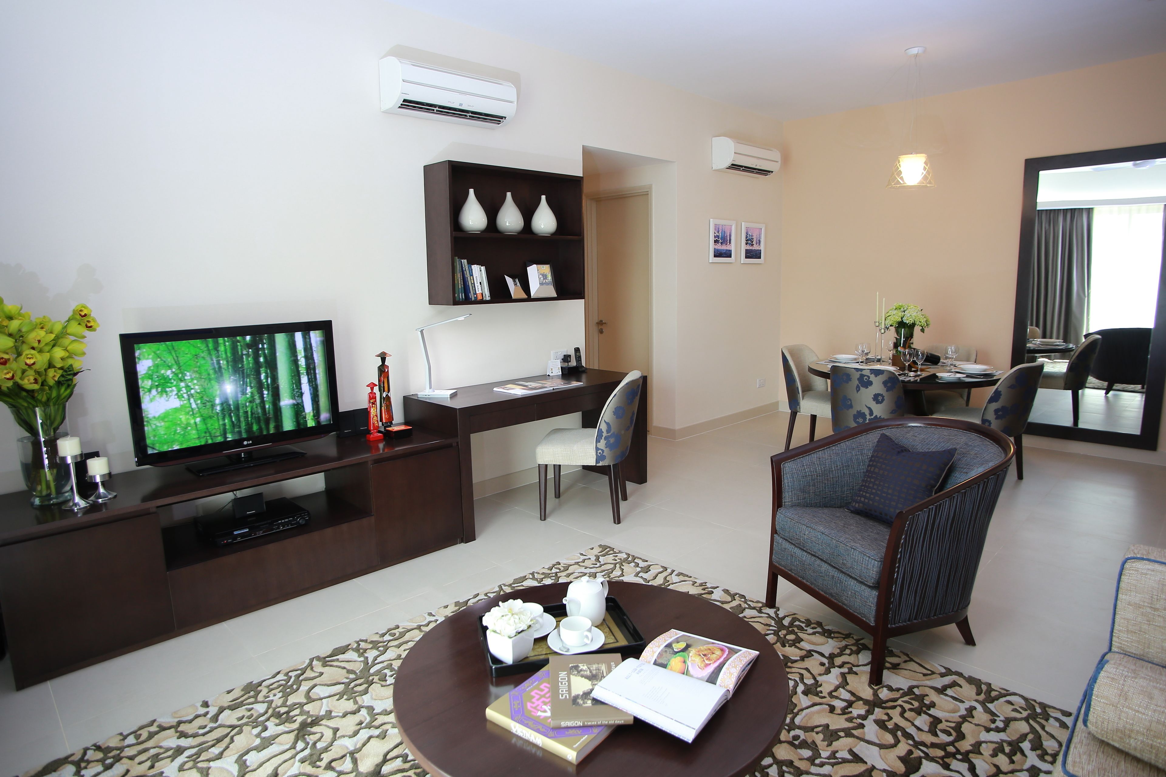 Una sala moderna con un televisor de pantalla plana, una mesa de centro con una revista, una estantería y un comedor con una mesa preparada para dos.