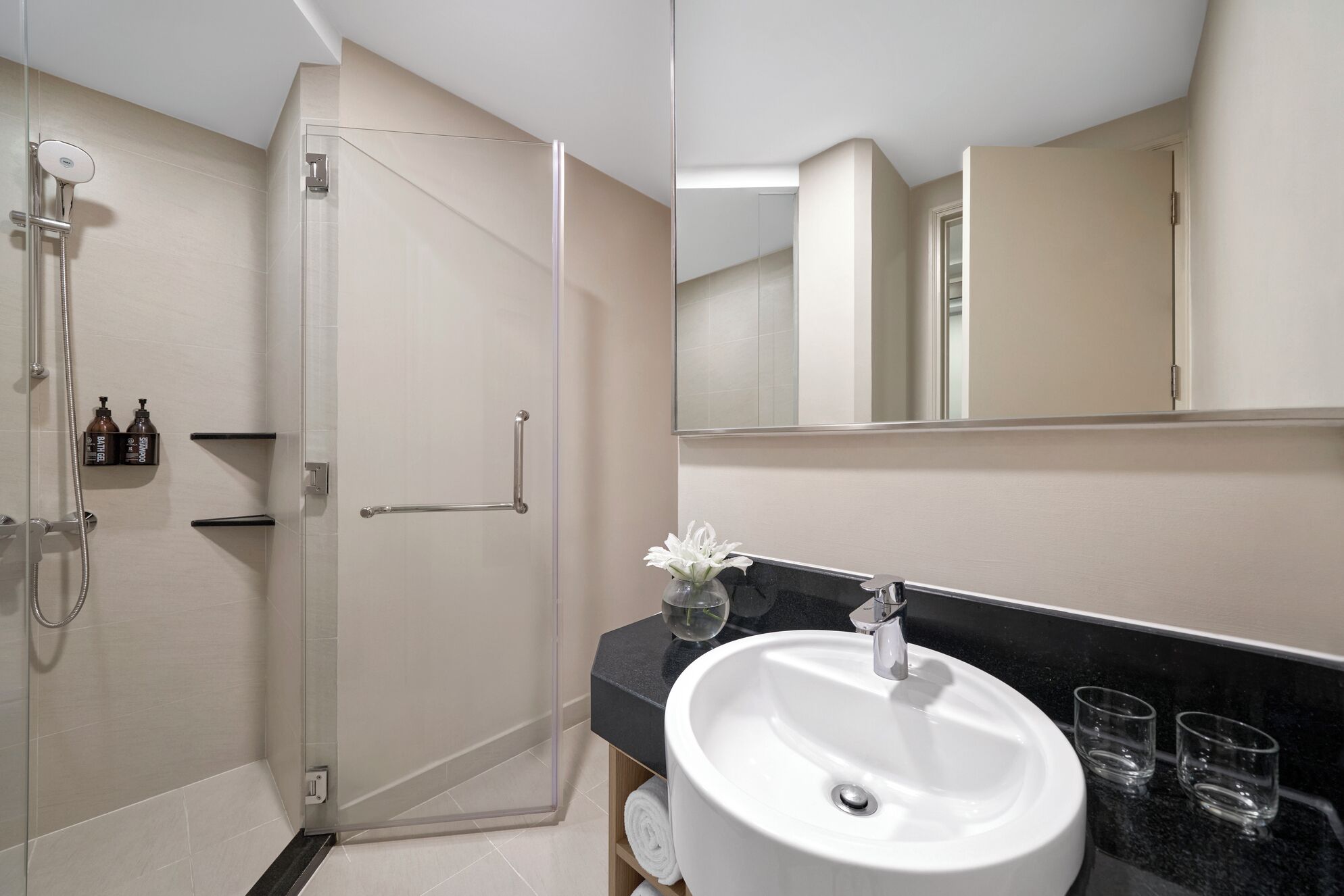 A modern bathroom with a glass-enclosed shower, a white sink, and a large mirror.