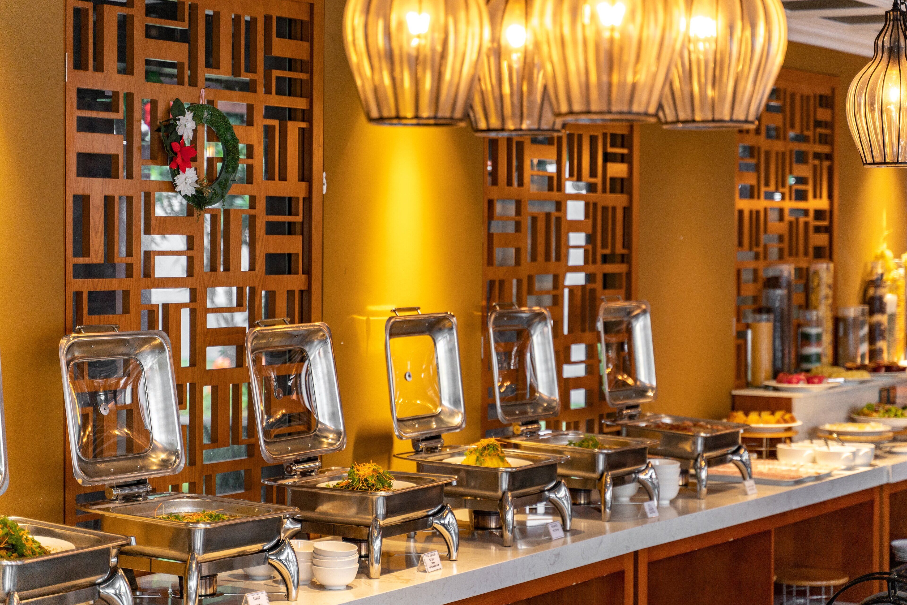 A buffet setup with multiple self-service stations, a decorative wreath, and a wooden partition with a geometric pattern.