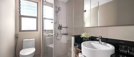 A modern bathroom with a toilet, glass-enclosed shower, and a sink with a mirror above.