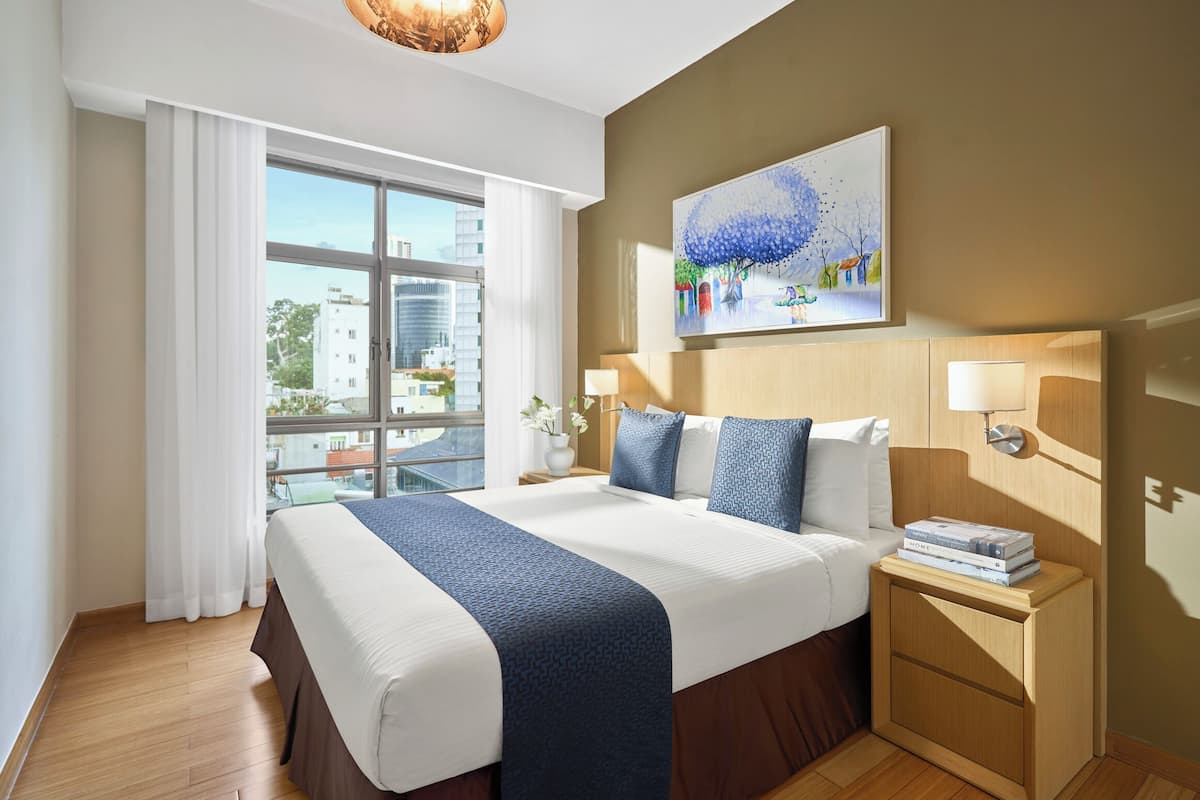 Una habitación de hotel moderna con una cama grande, una mesita de noche, un cuadro y vistas de la ciudad a través de la ventana.