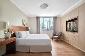 A hotel room with a bed, a TV, a chair, a desk, and a window with a city view. - Somerset Chancellor Court Ho Chi Minh City (Ho Chi Minh City)