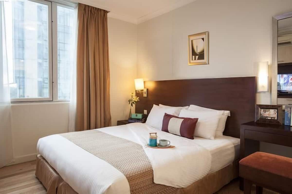 A hotel room with a large bed, a bedside table with a lamp, a window with curtains, and a framed picture on the wall.
