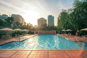 A swimming pool with a tiled deck, surrounded by lounge chairs and umbrellas, with buildings in the background. - Somerset Chancellor Court Ho Chi Minh City (Ho Chi Minh City)