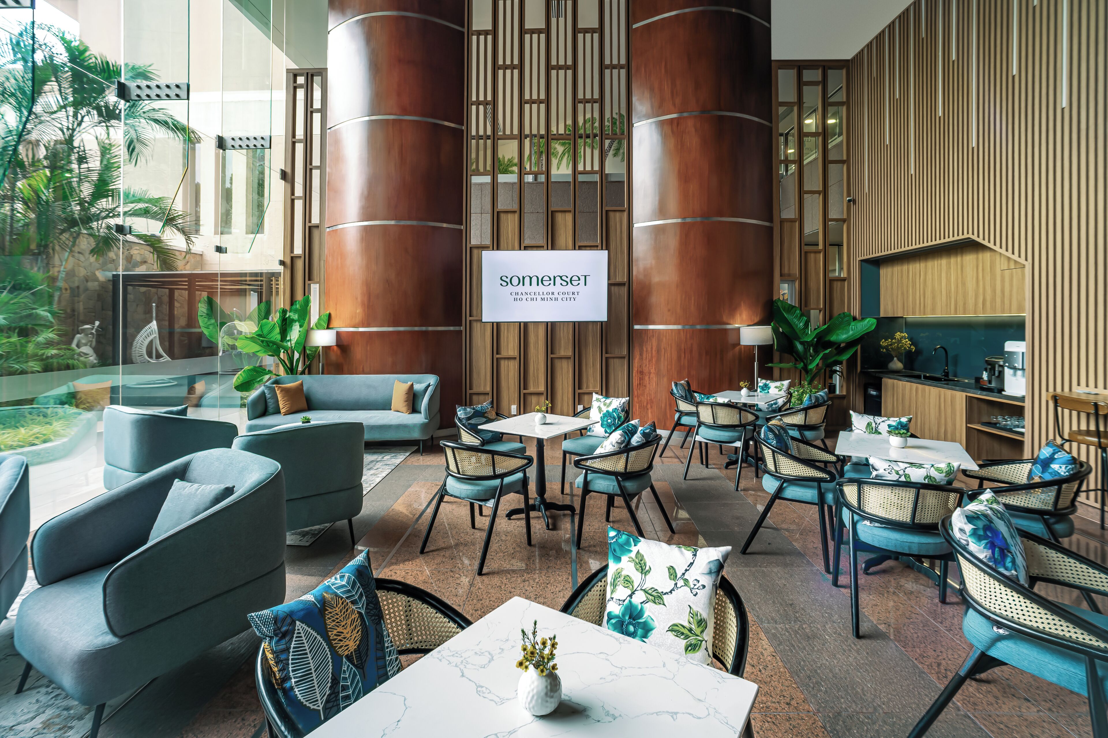 A modern interior with seating areas, a sign reading 'somerset CHANCELLOR COURT,' and a view of greenery outside.