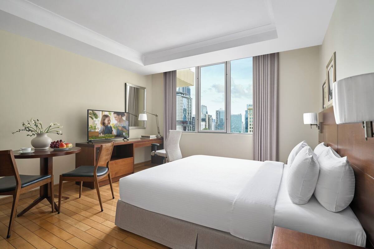 A hotel room with a bed, desk, chair, and a city view.