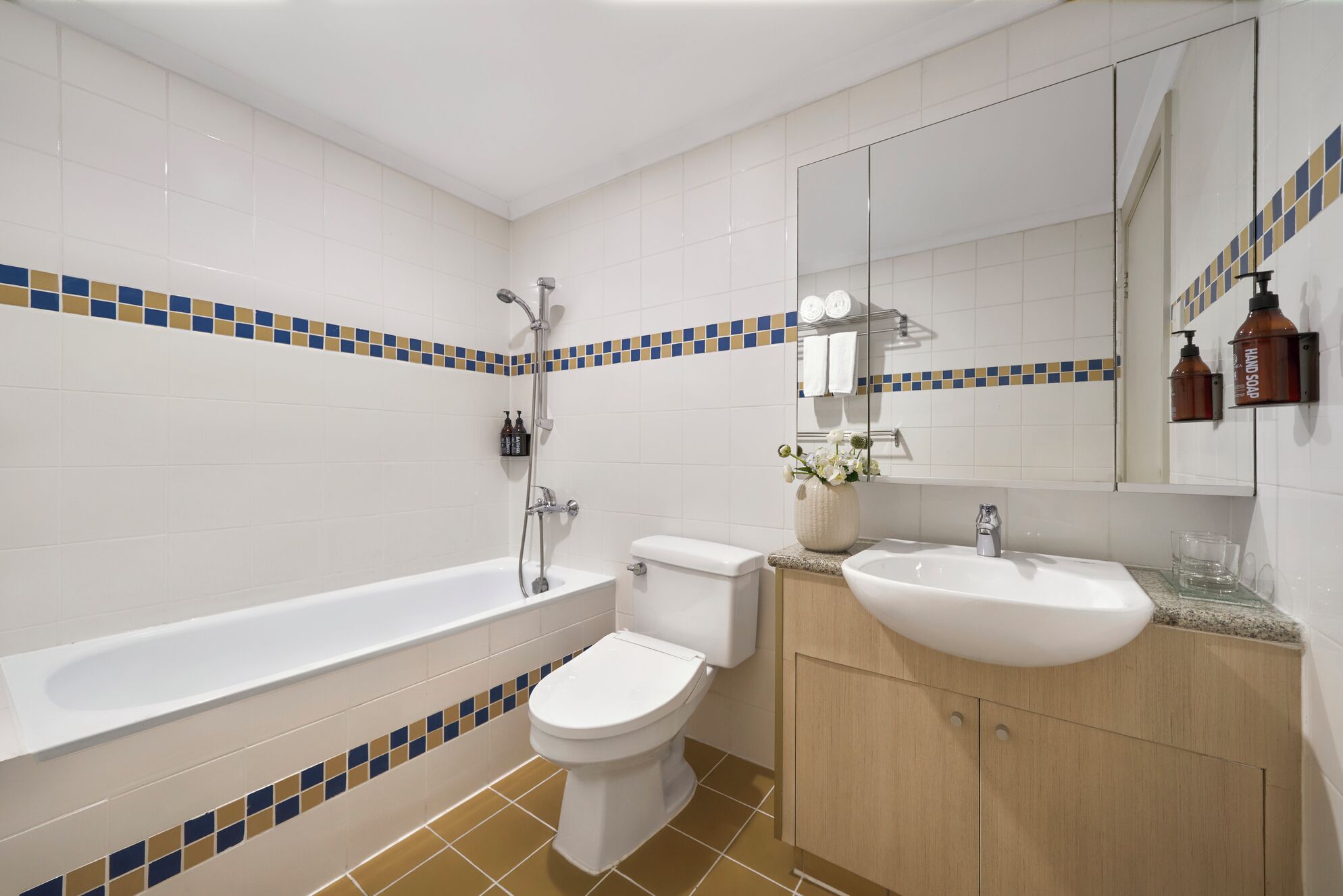 A bathroom with a bathtub, toilet, and sink, featuring a tiled backsplash with a blue and beige pattern.