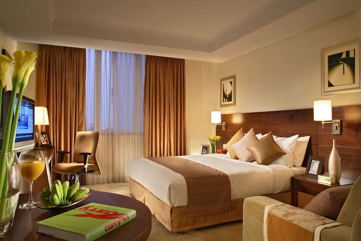 A hotel room with a bed, bedside tables, a desk with a chair, a lamp, a television, and a window with curtains.