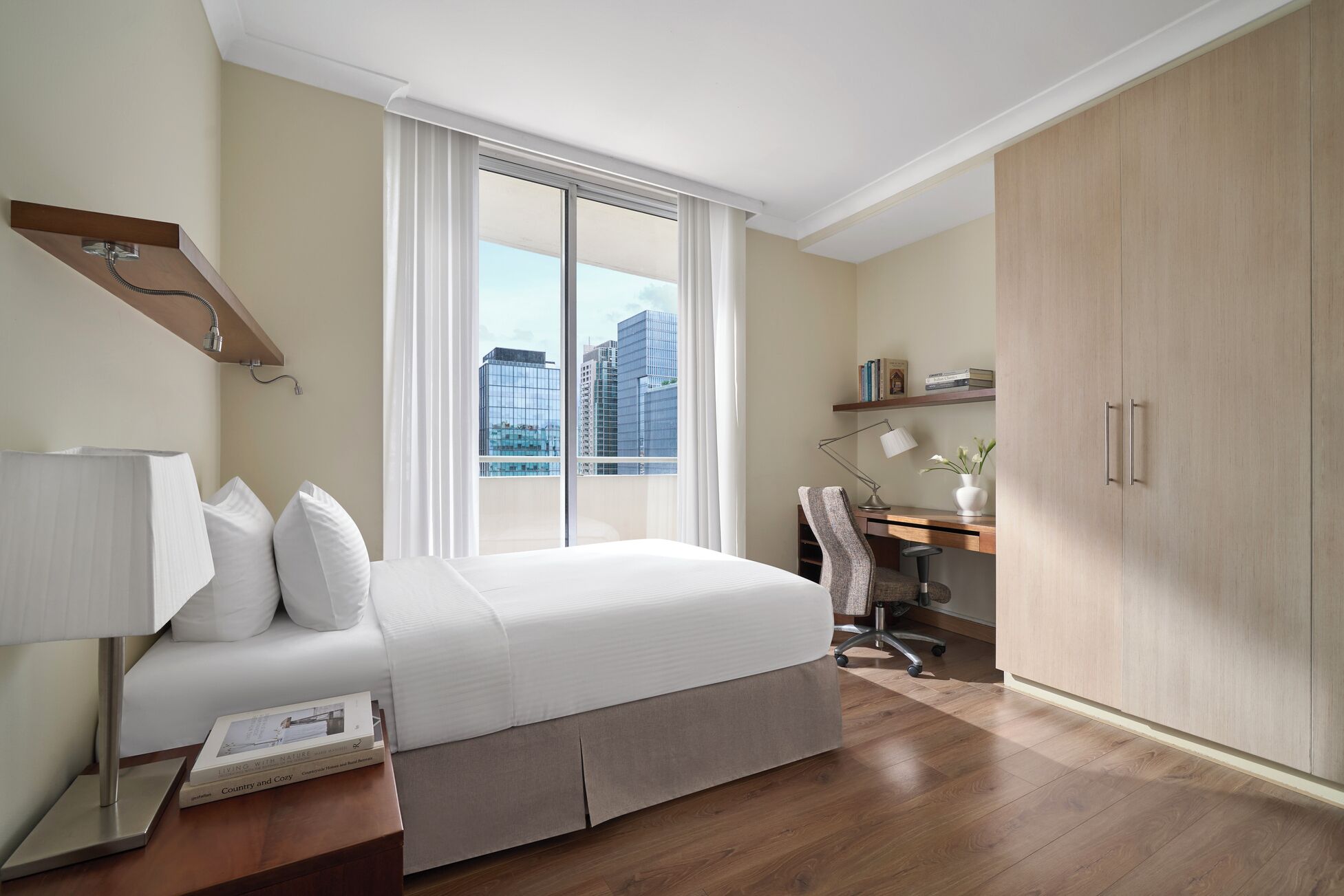 Une chambre d’hôtel équipée d’un lit, d’un bureau, d’une chaise, d’une armoire et d’une fenêtre donnant sur la ville.
