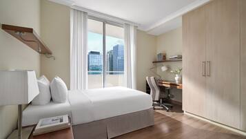 Une chambre d’hôtel équipée d’un lit, d’un bureau, d’une chaise, d’une armoire et d’une fenêtre donnant sur la ville.