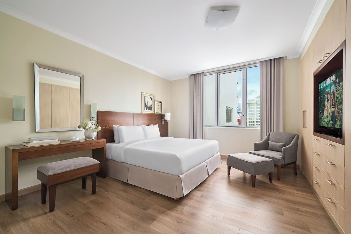 A hotel room with a bed, a desk, a chair, a TV, and a large window.
