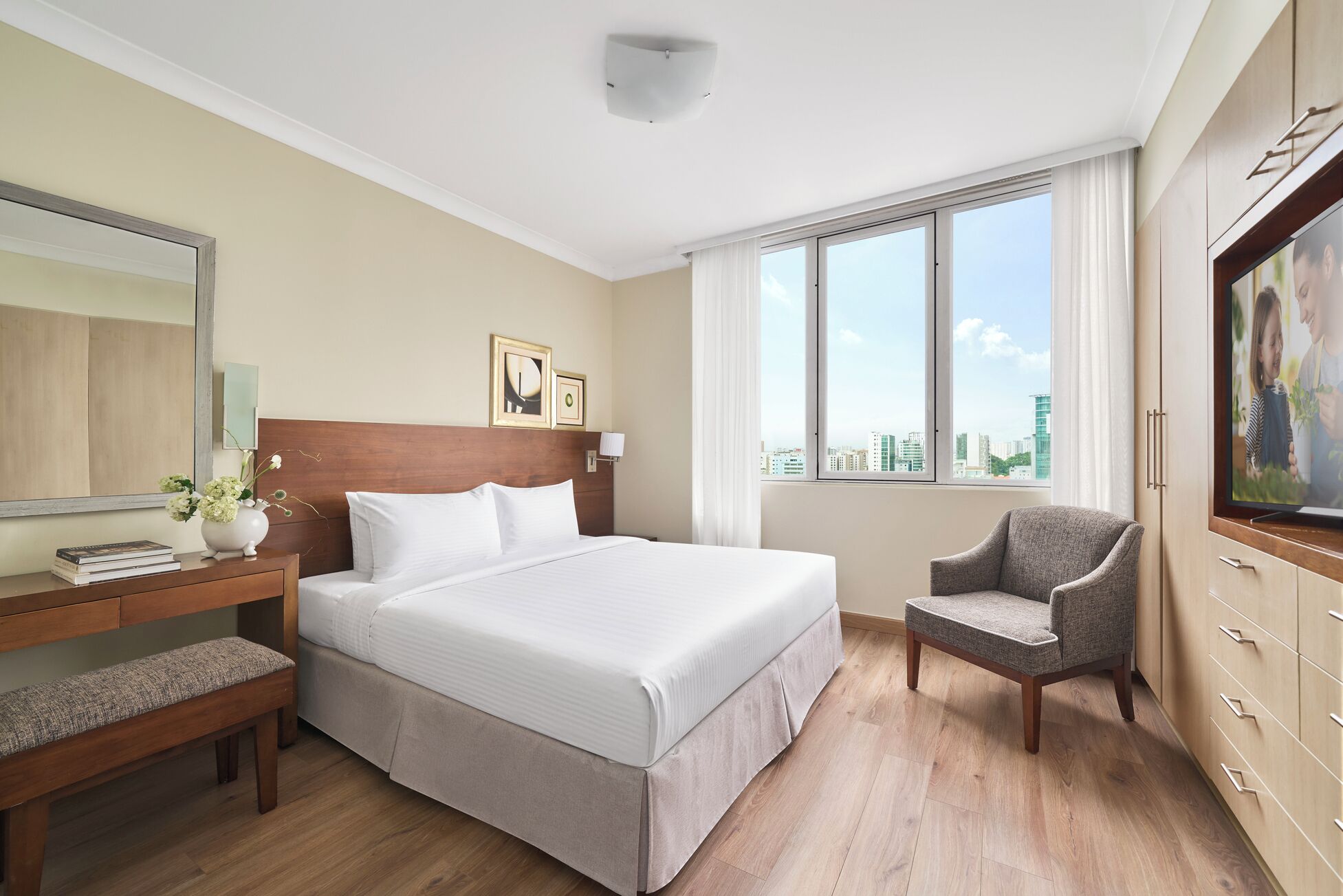 Ein Hotelzimmer mit Bett, Sessel, Schreibtisch mit Lampe, Spiegel und Fenster mit Stadtblick.