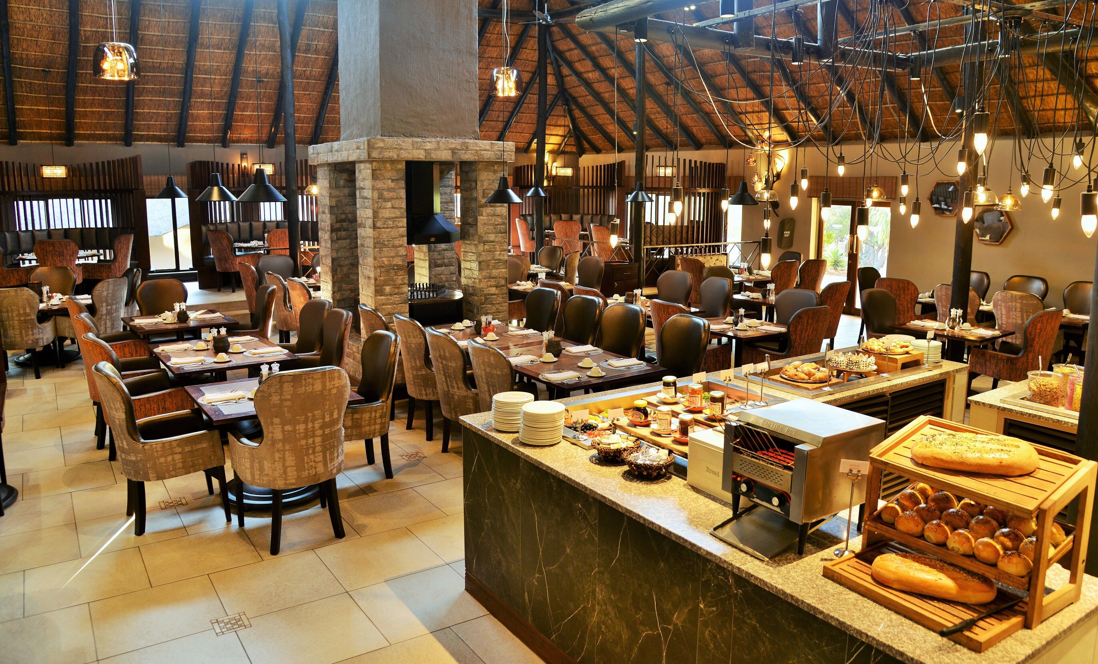 Een restaurant met meerdere eettafels en stoelen, een centraal eiland met brood en gebak, en hangende吊灯.