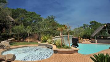 Relax by the serene pool surrounded by lush greenery and tropical plants, with a hot tub and walkway nearby.